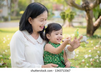 Asian Grandmother and granddaughter sitting and playing hand puppet together in the garden.Happy Asian family conception. - Powered by Shutterstock