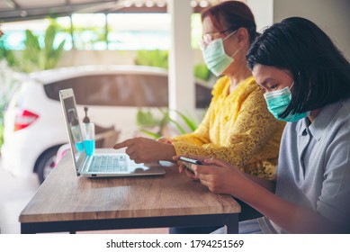 Asian Grandmother And Kid Wear Mask And Using Mobile Phone Together. Thai Elderly Woman And Child Sitting And Learn Online Study At Home. Happy Family In New Normal Lifestyle Concept.