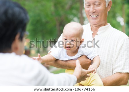 Asian grandparents playing with baby grandson at outdoor garden.