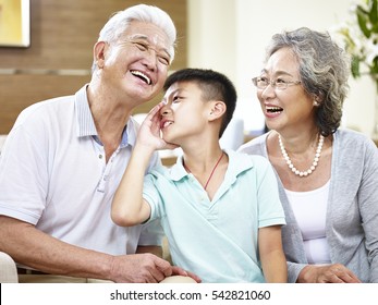 Asian Grandson Whispering To Grandfather While Grandmother Watching.