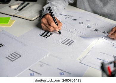 Asian graphic designer making notes on logo designs, using computers, designing logos, and showcasing the corporate identity and logo design process.	
