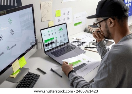 Asian graphic designer making notes on logo designs, using computers, designing logos, and showcasing the corporate identity and logo design process.	