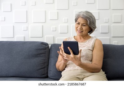 Asian Gray Hair Old Woman Looking At Tablet Computer Monitor, Smiling While Sit On Sofa In The Living Room.