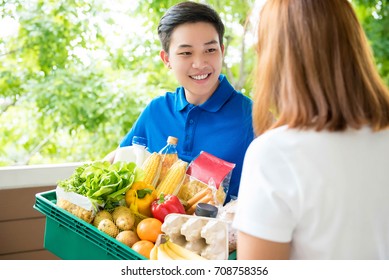 An Asian Grocery Store Delivery Man Wearing A Blue Poloshirt Delivering Food To A Woman At Home