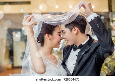 Asian groom and Asian bride are under viel together and are about to kiss each other with a smiling and happy face.