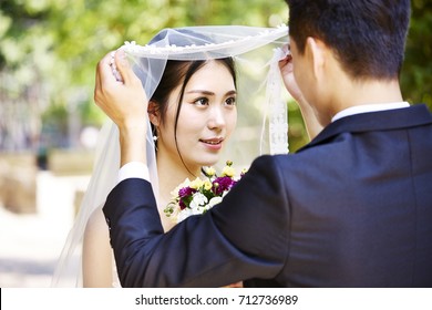 asian groom lifting up bridal veil to kiss beautiful bride. - Powered by Shutterstock