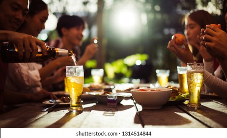 Asian Group Eating And Drinking Cold Beer Outside The House At Night, Having Fun Talking