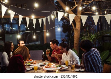 Asian Group Eating And Drinking Cold Beer Outside The House At Night, Having Fun Talking