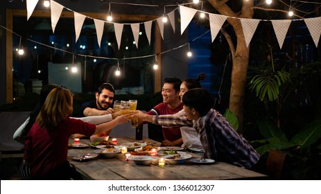 Asian Group Eating And Drinking Cold Beer Outside The House At Night, Having Fun Talking