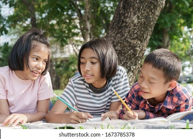 Asian Group Elementary School Children Write A Notebook With A Pencil And Learning Together In The Summer At Park In The Morning. The Student Came To Study Field Trip And  Activity Learned Outdoor