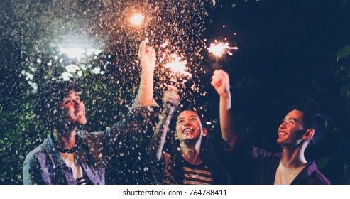 Asian group of friends having outdoor garden barbecue laughing with alcoholic beer drinks and showing group of friends having fun with sparklers on night ,soft focus - Powered by Shutterstock