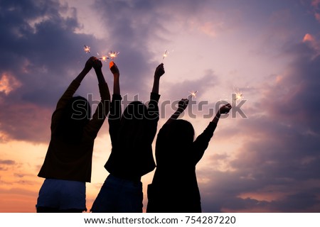 Asian group of friends lighting sparklers and enjoying freedom at sunset,Silhouette of asian woman holding sparklers happily at colorful sky