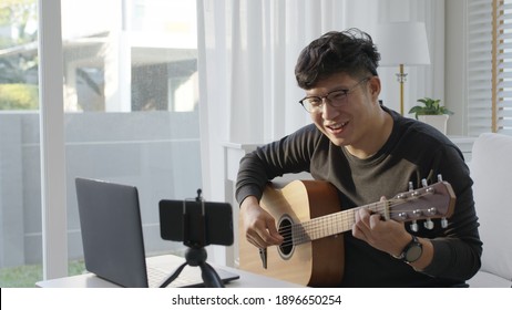 Asian Guitarist Livestream Video Or Virtual Video Tutorial At Home,artist Musician Blogger Or Vlogger Sit On Sofa In The Living Room Explaining To Play Guitar,online Learning During Quarantine Concept