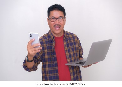 Asian guy in casual clothes, standing with laptop and smartphone in his hands ready to work from home
