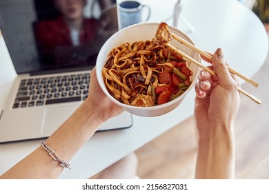 Asian Guy Eating Instant Noodles While Working On Laptop At His Home Office