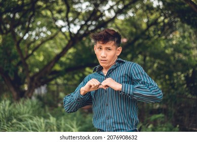 An Asian Guy In His 20s Pointing Towards Himself With A Worried Look. Reaction From Being Accused Of Something. Outdoor Scene.