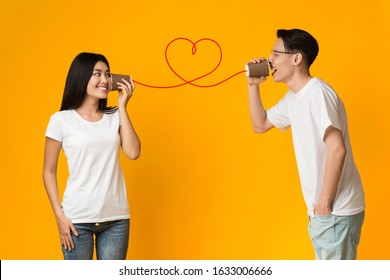 Asian guy telling his girlfriend about love, using can phone, orange background