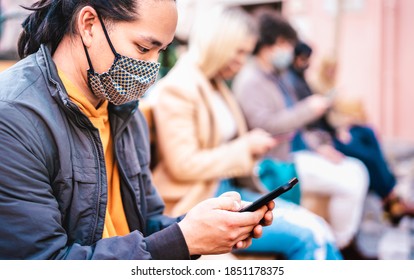 Asian guy using smart phone covered by face mask on Covid second wave - New normal lifestyle concept with milenial people watching news on mobile smartphone - Shallow depth of field with focus on man - Powered by Shutterstock