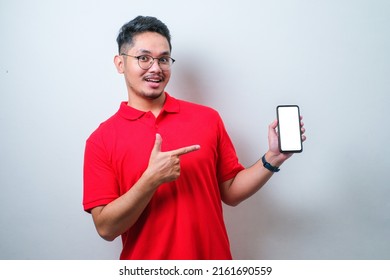 Asian Guy Wearing Red Shirt Smile Looking To Camera Showing Smartphone Empty Screen Recommending Application, Isolated On White Background