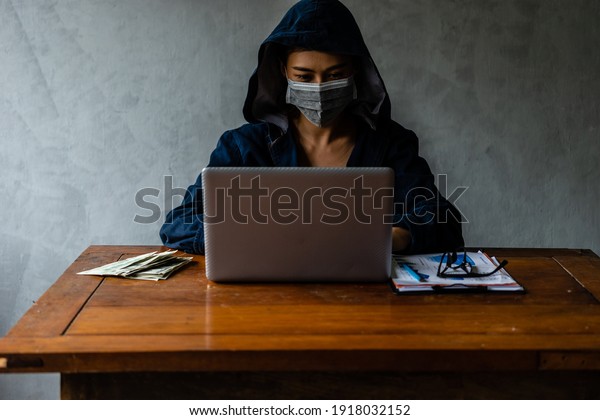 Asian hacker woman with surgical facemask typing\
on laptop notebook