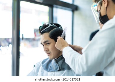 Asian Hairdresser Barber Wear Mask, Cut Hair Of Attractive Man In Shop. Handsome Young Man Customer In Modern Salon Barbershop, Enjoy Getting Haircut Service By Stylist Man During Covid 19 Pandemic.