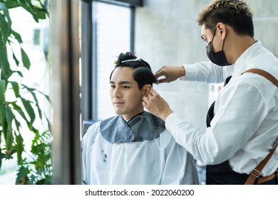 Asian Hairdresser Barber Wear Mask, Cut Hair Of Attractive Man In Shop. Handsome Young Man Customer In Modern Salon Barbershop, Enjoy Getting Haircut Service By Stylist Man During Covid 19 Pandemic.