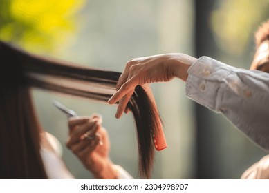 Asian Hairdresser giving treatment and barber occupation service, Professional hairstylist combing and using scissors cut woman's hair to young beautiful customer girl in beauty salon - Powered by Shutterstock