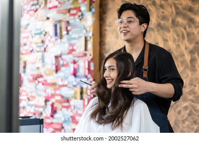 Asian hairstylist male combing and using scissors cut woman's hair. Professional Hairdresser or barber giving treatment and occupation service to smiling young beautiful girl customer in beauty salon.