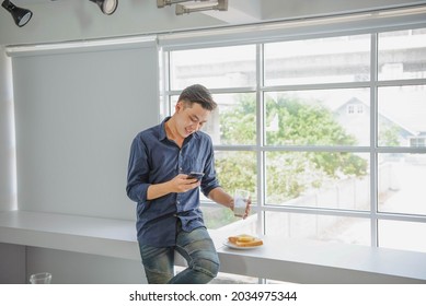 asian handsom business man taking to mobile phone and holding glass of milk in white modern office