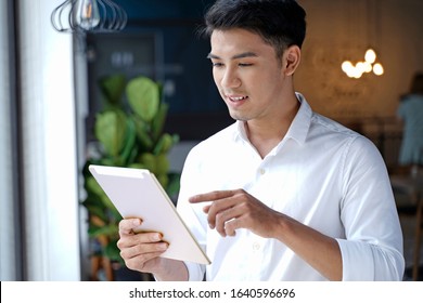 Asian handsome businessman or office worker or young student using laptop computer at office shop with green plant and open space - Powered by Shutterstock