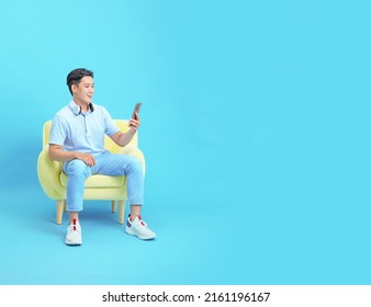 Asian Handsome And Cheerful Young Man Sitting On Relaxing Sofa, Isolated On Background