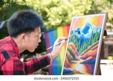 Asian handsome gay wears rainbow wristband and reparing his art mountain drawing in the park, concept for lifestyle and recreational activity of LGBT people around the world, new edited.