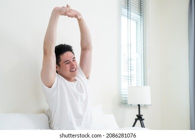 Asian Handsome Male In Pajamas Wake Up In The Morning With Happiness. Attractive Young Man Smiling, Feeling Happy And Relax Then Stretching Body After Getting Up From Sleep On Bed In Bedroom At Home.