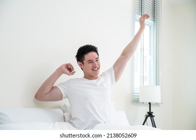 Asian Handsome Male In Pajamas Wake Up In The Morning With Happiness. Attractive Young Man Smiling, Feeling Happy And Relax Then Stretching Body After Getting Up From Sleep On Bed In Bedroom At Home.