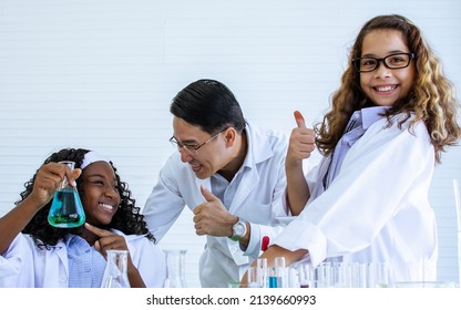 Asian Handsome Male Teacher Wearing Eyeglasses And White Gown Uniform, Teaching Science And Experiment To African Black And Caucasian White Female Students In Classroom At School. Education Concept