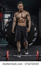 Asian handsome man posting with dumbbells in dark gym