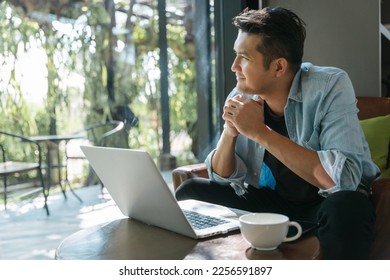 Asian handsome man sitting happily looking out of the window in a cafe. Concept freelance and financial freedom.