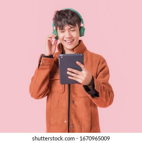 Asian handsome man smiling and listening music by big green headphones by smartphone search. Happy boy from listen to music using wireless technology in to smartphone isolated on pink background. - Powered by Shutterstock