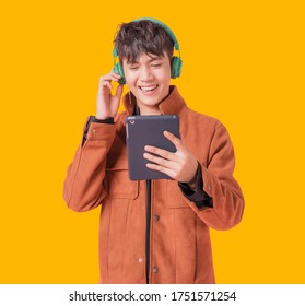 Asian handsome man smiling and listening music by big green headphones by smartphone search. Happy boy from listen to music using bluetooth technology in to smartphone isolated on yellow background. - Powered by Shutterstock