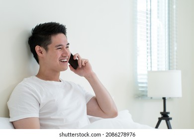 Asian Handsome Man Talk On Mobile Phone Call On Bed At Home In Morning. Happy Attractive Male Lying Down In Bedroom Enjoy Holiday Weekend, Using Smartphone Communication With Technology In House.