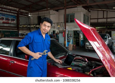 Asian Handsome Mechanic Using Laptop Computer Checking Car At Garage.