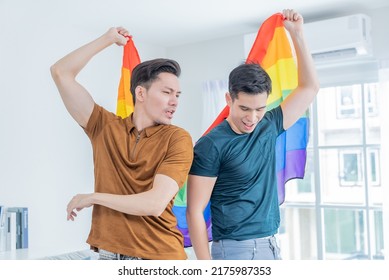 Asian Handsome Men Gay Family Holding LGBTQ Flag And Dancing Together. Attractive Romantic Male Lgbt Couple Spending Time And Enjoy Listen To Music, Have Fun With Gay Pride Feel And Carry Rainbow Flag