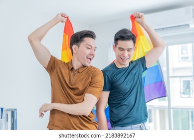 Asian Handsome Men Gay Family Holding LGBTQ Flag And Dancing Together. Attractive Romantic Male Lgbt Couple Spending Time And Enjoy Listen To Music, Have Fun With Gay Pride Feel And Carry Rainbow Flag