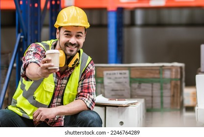 Asian handsome professional male worker smiling, holding cup of coffee, taking rest after work in storage, warehouse or factory for delivery, wearing safety hat. Commercial Industry Business Concept - Powered by Shutterstock