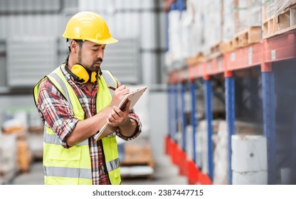 Asian handsome professional male worker holding board, checking shipping stocks in storage, warehouse or factory for delivery, wearing safety hat. Commercial Industry Business Concept - Powered by Shutterstock