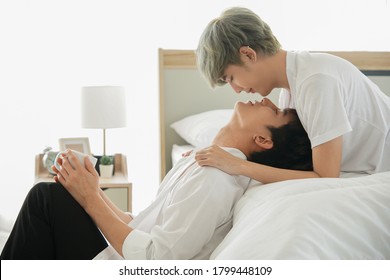 Asian Handsome Young Gay Couple Kissing Lying On The Bed And Holding Cup Of Coffee In The Morning