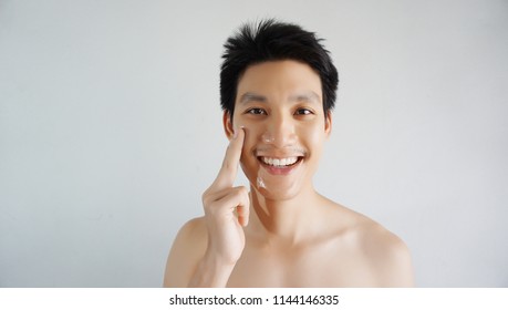 Asian handsome young  man applying cream at his face with smiley face, Skin care concept ,isolated on white background                             