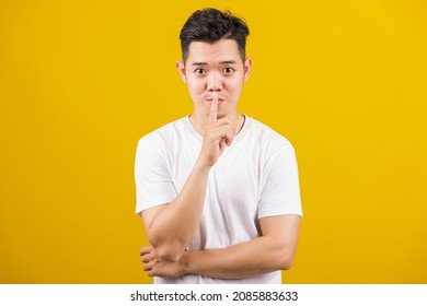 Asian Handsome Young Man Holding Index Finger On Lips Asking For Silence Or Secret Gesturing, Studio Shot Isolated On Yellow Background, Making Shh Shush Gesture Concept