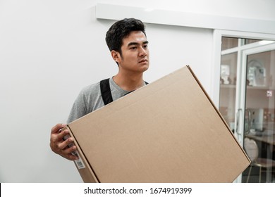 Asian Handyman Carrying A Big Box. Delivery Man Lifting A Box Of Good. Man Holding Heavy Package For Moving Service. Hand Transportation.