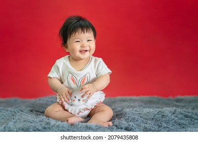 Asian Happy Baby Smiling And Sitting On Red Color Background. Cute 6 Months Baby With Copy Space Use As Concept Of Bedroom, Drypers, Development, Baby Or Kid Department In Hospital.